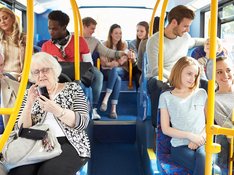 Menschen verschiedenen alters sitzen in einem Bus. Ansicht von innen, Mittelgang nach hinten.