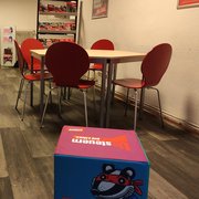 Neue Büroeinrichtung: im Vordergrund ein Sitzwüfel, mit Motiven der Umsteuern-Kampagne, dahinter eine Sitzgruppe im 6-Eck, Tisch mit Buchendekor, mit roten Stapelstühlen