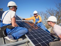 Drei Arbeiter montieren Photovoltaik-Paneele auf einem Dach