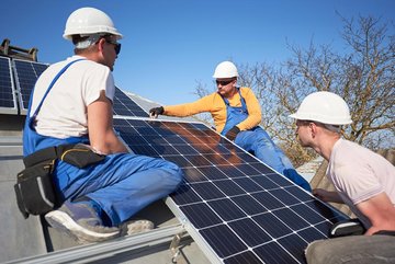 Drei Arbeiter montieren Photovoltaik-Paneele auf einem Dach